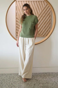 Women wearing a green mock neck sweater with pocket detail and wide-leg cream pants