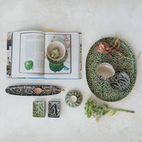 Stoneware dish with botanical wax relief featuring open cookbook with tropical fruit recipe