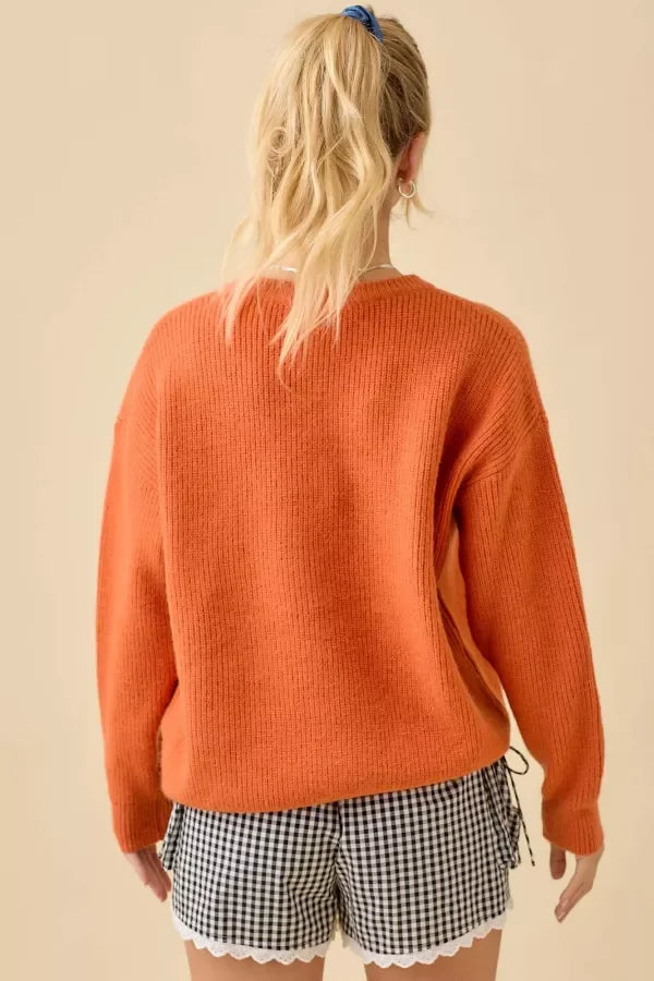 Orange knit sweater with pumpkin face patchwork and black and white gingham shorts