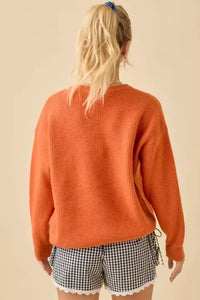 Orange knit sweater with pumpkin face patchwork and black and white gingham shorts