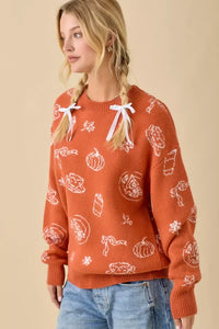 Orange pumpkin spice printed sweater with fall-themed patterns and shoulder ribbon ties
