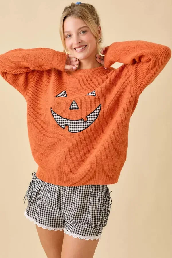 Orange long-sleeved sweater with pumpkin face patchwork and black and white gingham design