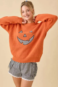 Orange long-sleeved sweater with pumpkin face patchwork and black and white gingham design