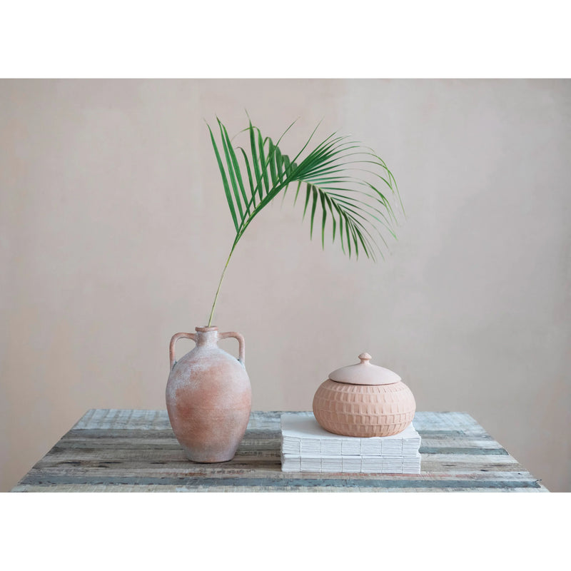 Boho decor featuring a palm frond in a vase with a lidded container on weathered wood