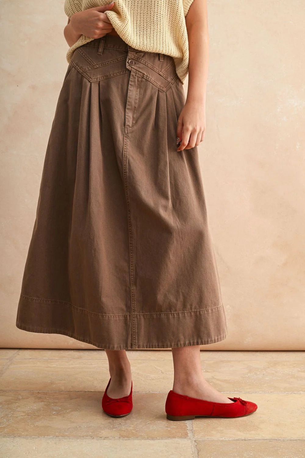 Person wearing a mini pleat detailed long skirt with a light yellow knitted top and red ballet flats