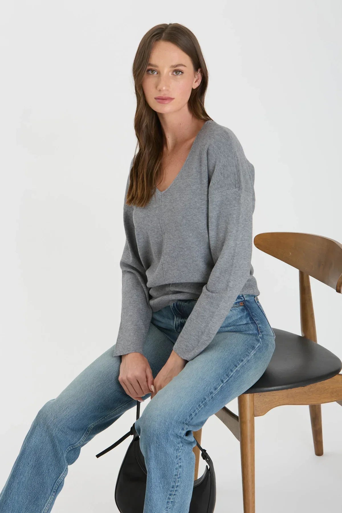 Person in gray seam knit sweater and blue jeans sitting on a wooden chair