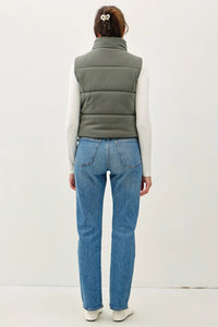 Person in a green puffer vest with zipper and blue jeans, showcasing boho style