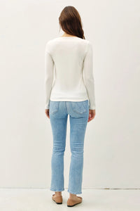 Person in a white long sleeve basic boat neck knit top and light blue jeans, back view