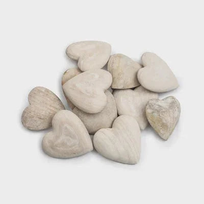 Carved wooden heart surrounded by a pile of white pebbles on a white background