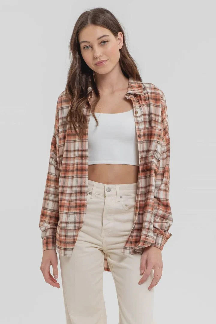 Long sleeve button down plaid shirt styled over a white crop top and light pants