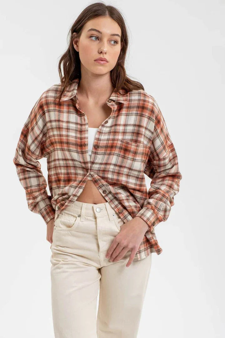 Long sleeve button down plaid shirt knotted in front over cream-colored pants