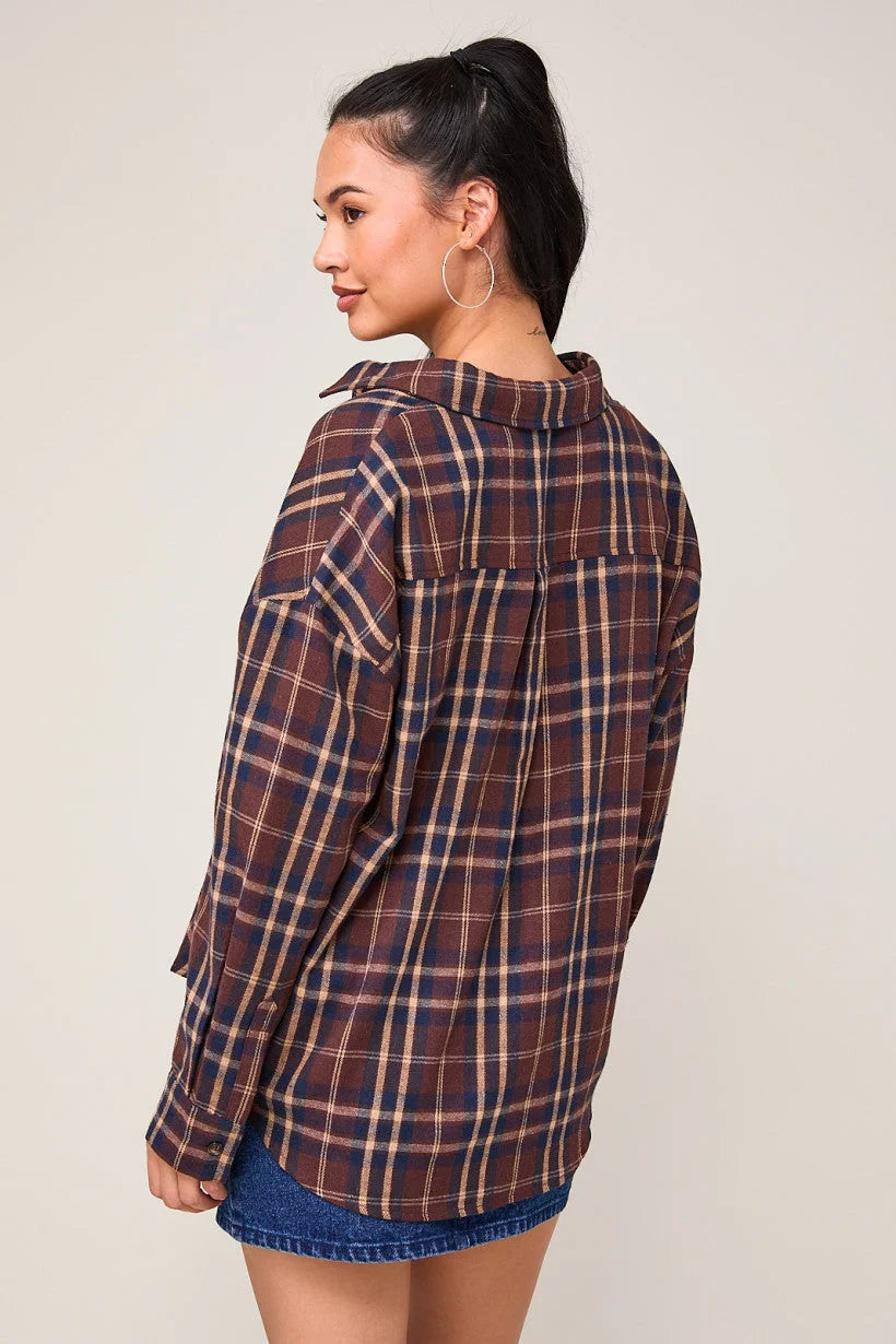 Woman with dark hair in a ponytail wearing an oversized plaid shirt top