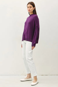 Purple oversized mock neck sweater with long sleeves worn over white pants