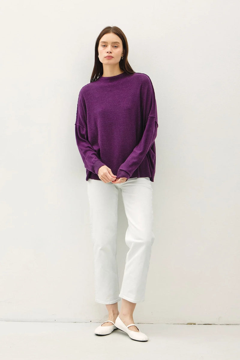 Purple oversized mock neck sweater styled with white pants and light-colored flats