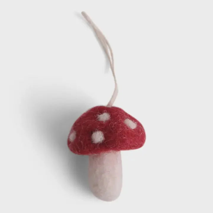 Handmade mini mushroom ornament with red felt, white polka dots, and cream stem hanging by string