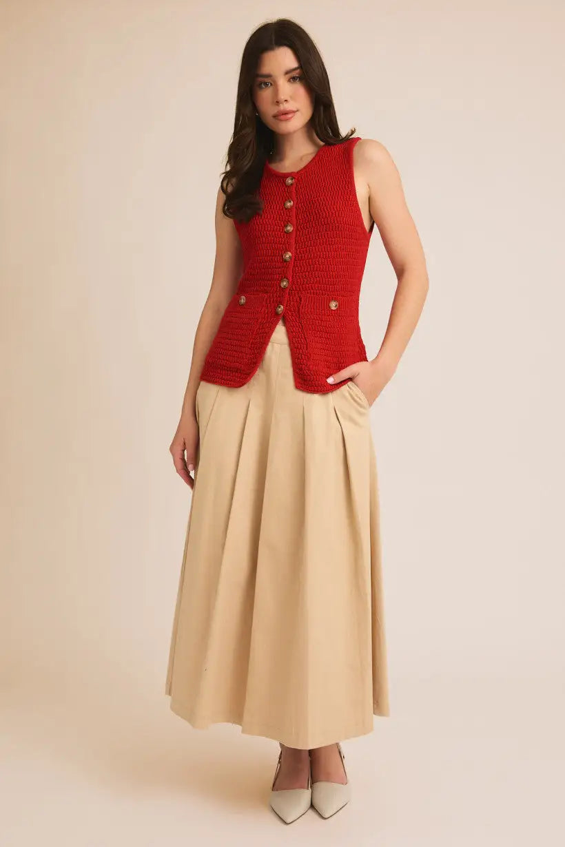 Red sweater vest paired with a beige pleated midi skirt from Shop Daisy’s boho chic collection