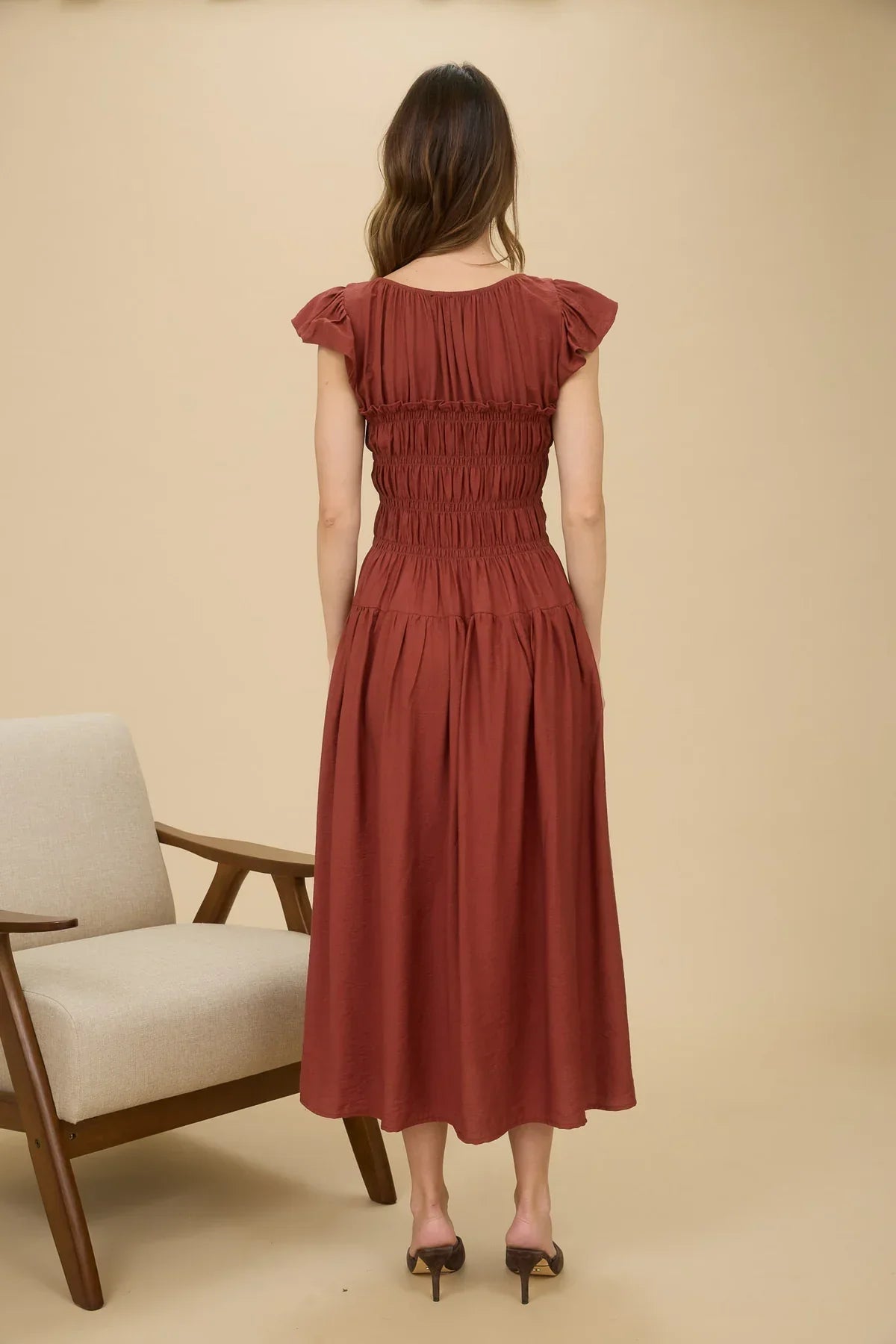 Woman modeling rust-colored midi dress with shirred bodice and ruffle sleeve detail