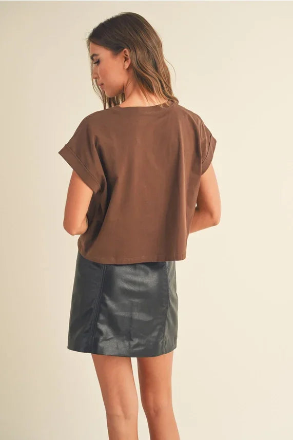 Round neck cuffed short-sleeved brown cropped T-shirt paired with a black faux leather mini skirt