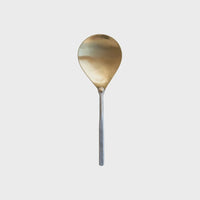 Brass serving spoon with a hammered aluminum handle elegantly displayed on a surface