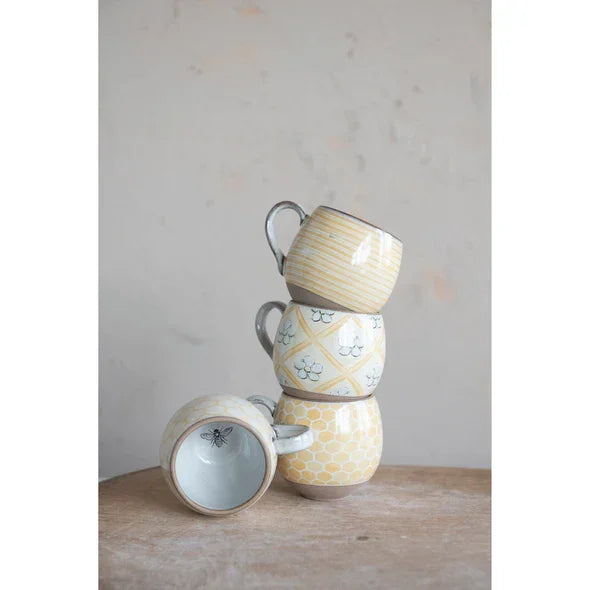 Stack of four pastel-colored ceramic stoneware mugs with floral patterns and bee designs