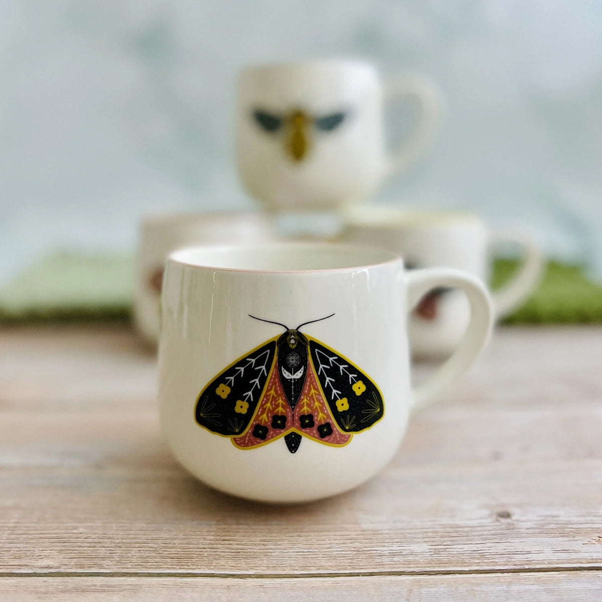 White stoneware mug with vibrant colored rim and colorful moth illustration