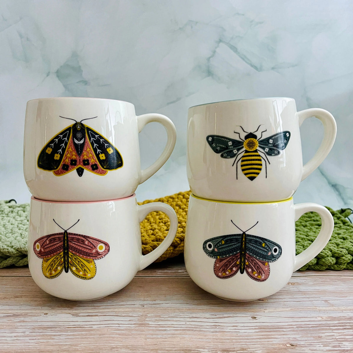 Four white stoneware mugs with vibrant colored rims and insect illustrations