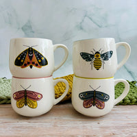 Four white stoneware mugs with vibrant colored rims and insect illustrations