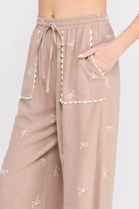 Taupe embroidered linen pants with bow pattern and scallop trim for a stylish look