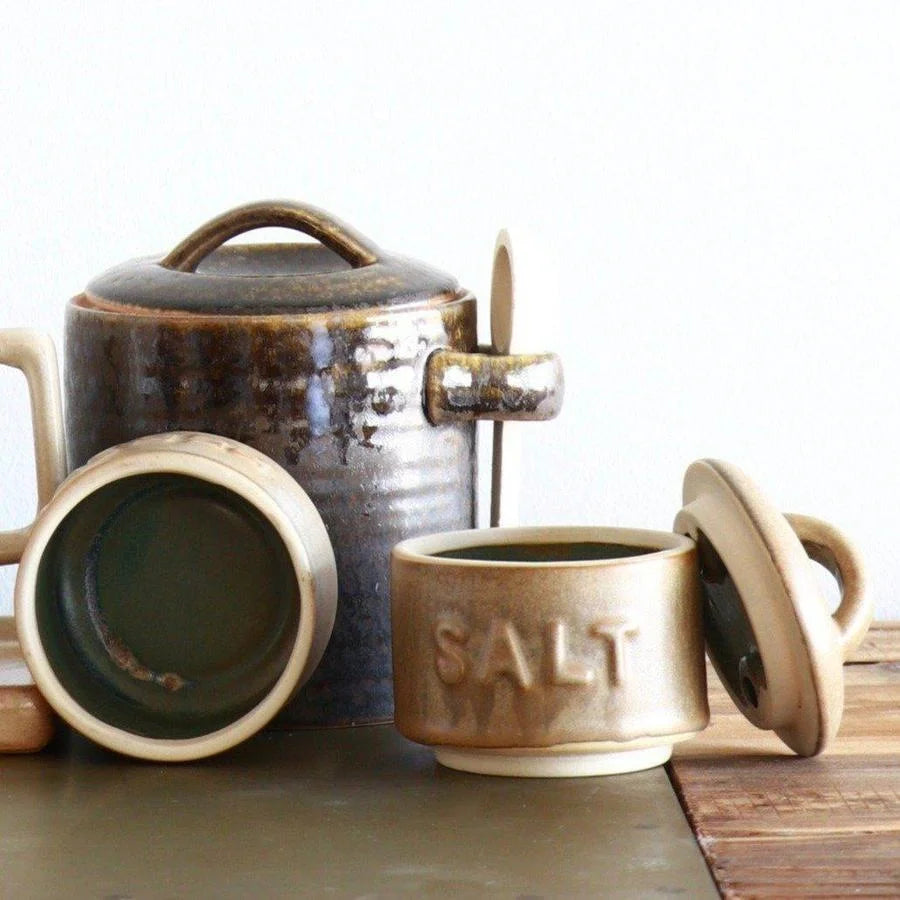 Stackable stoneware salt and pepper shakers beside a tea pot and cups on a table