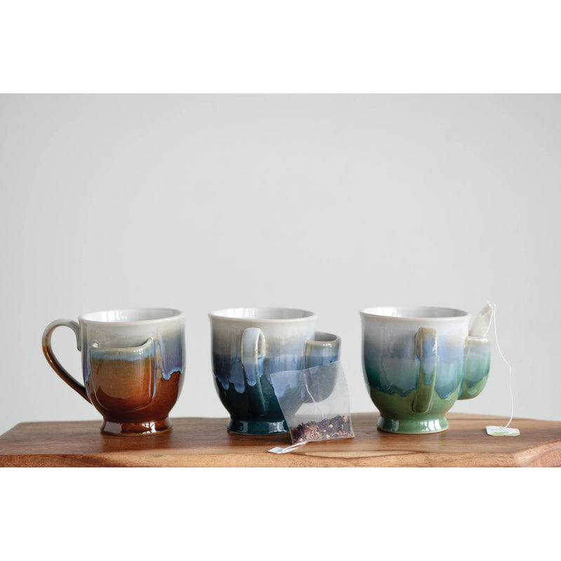 Three ceramic mugs with colorful glazes ideal for a tea bag holder beside a wooden surface