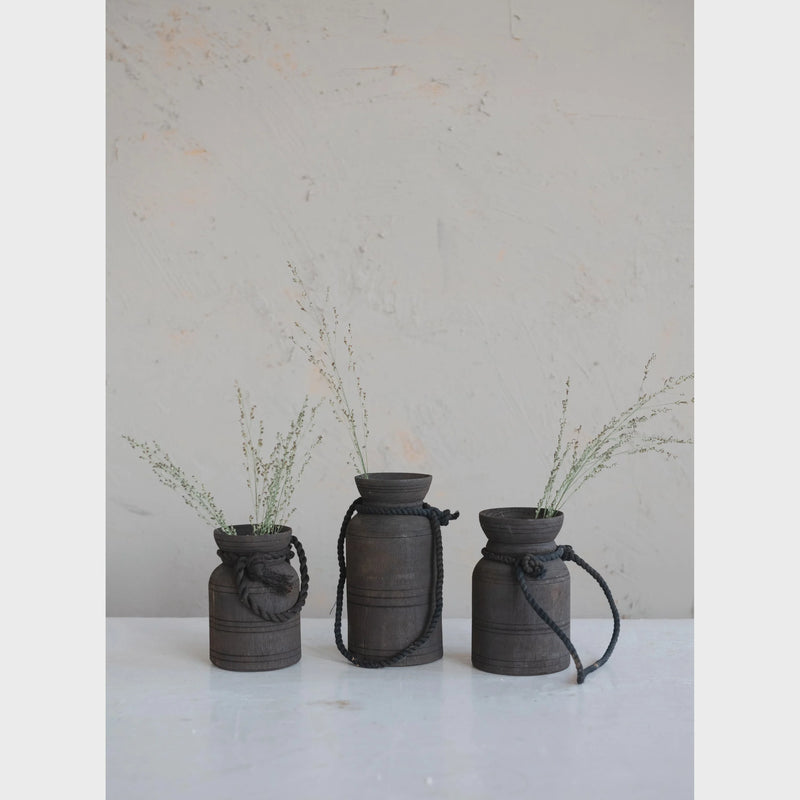 Decorative wood jug with dark cylindrical vases, rope accents, and dried plants