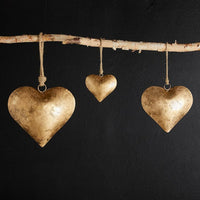 Three golden heart ornaments hanging from a birch branch of the Golden Antique Heart