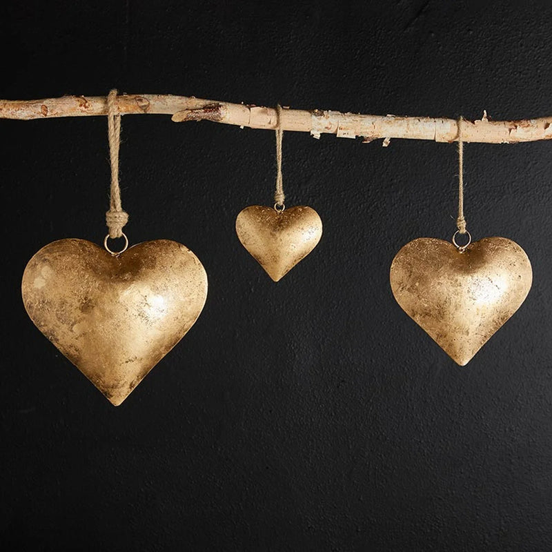 Three golden heart ornaments hanging from a birch branch of the Golden Antique Heart