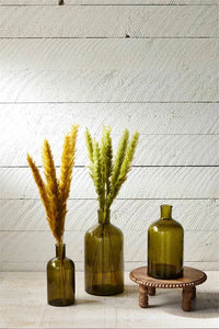 Three green glass bottles featuring dried pampas grass as elegant decor elements