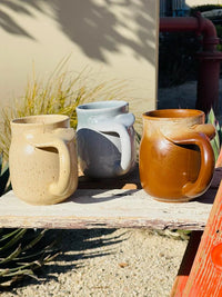 Three stoneware mugs with whale tail handles displayed on a bench