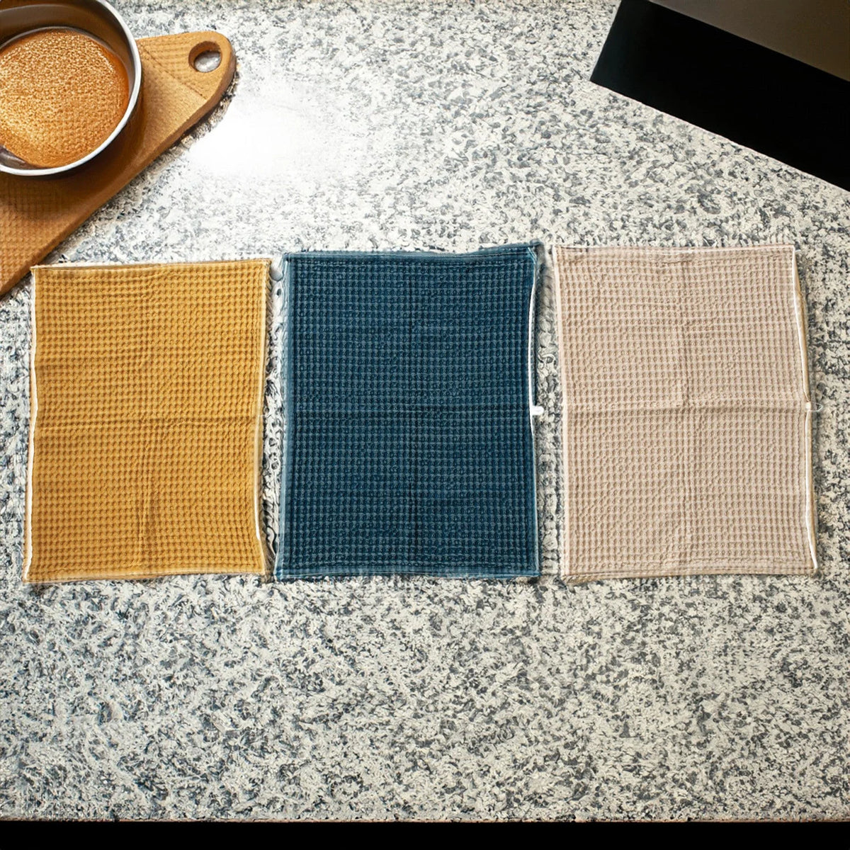 Three waffle cotton tea towels in yellow, teal, and beige with a boho design