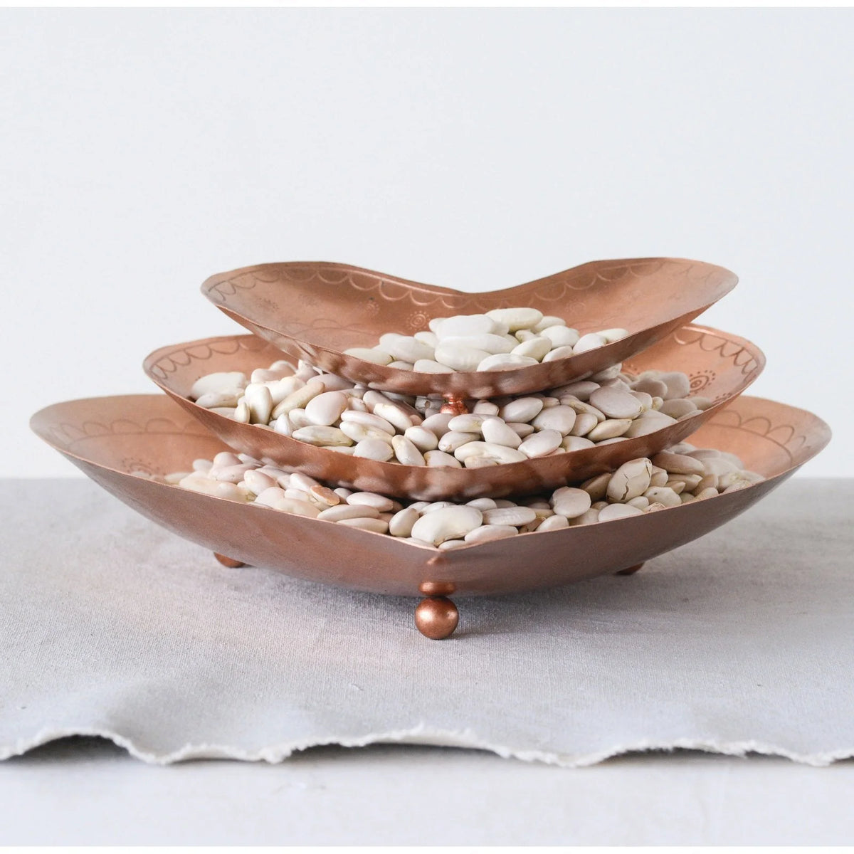 Three-tiered copper tray filled with white stones, featuring embossed metal details