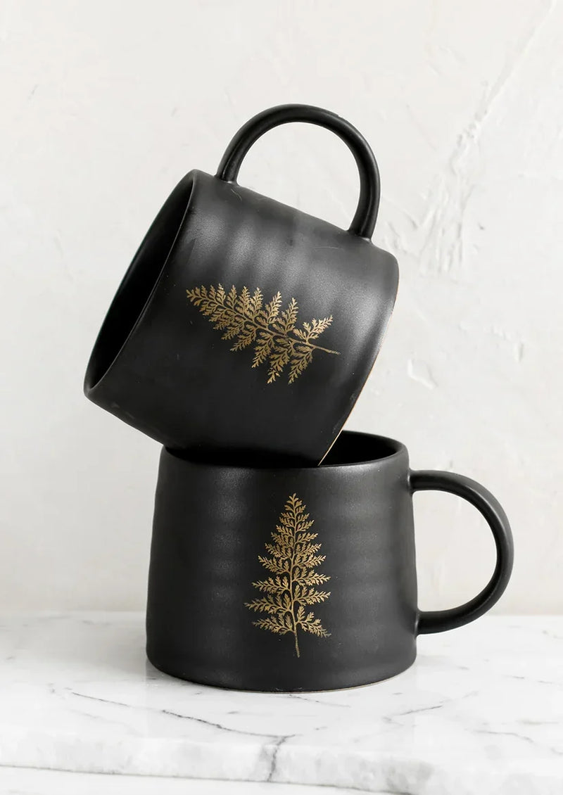 Two black ceramic coffee mugs with golden fern designs, showcasing botanical print ceramic design