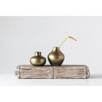 Two antique brass debossed metal vases on a weathered wooden block setting