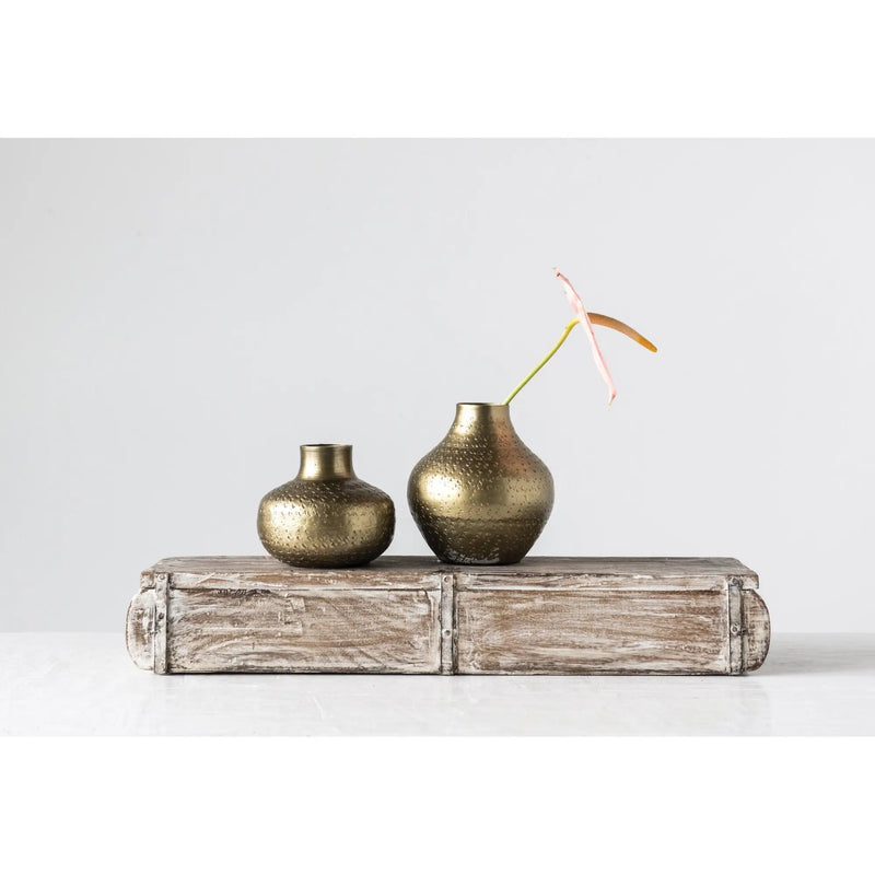 Two antique brass debossed metal vases on a weathered wooden block setting