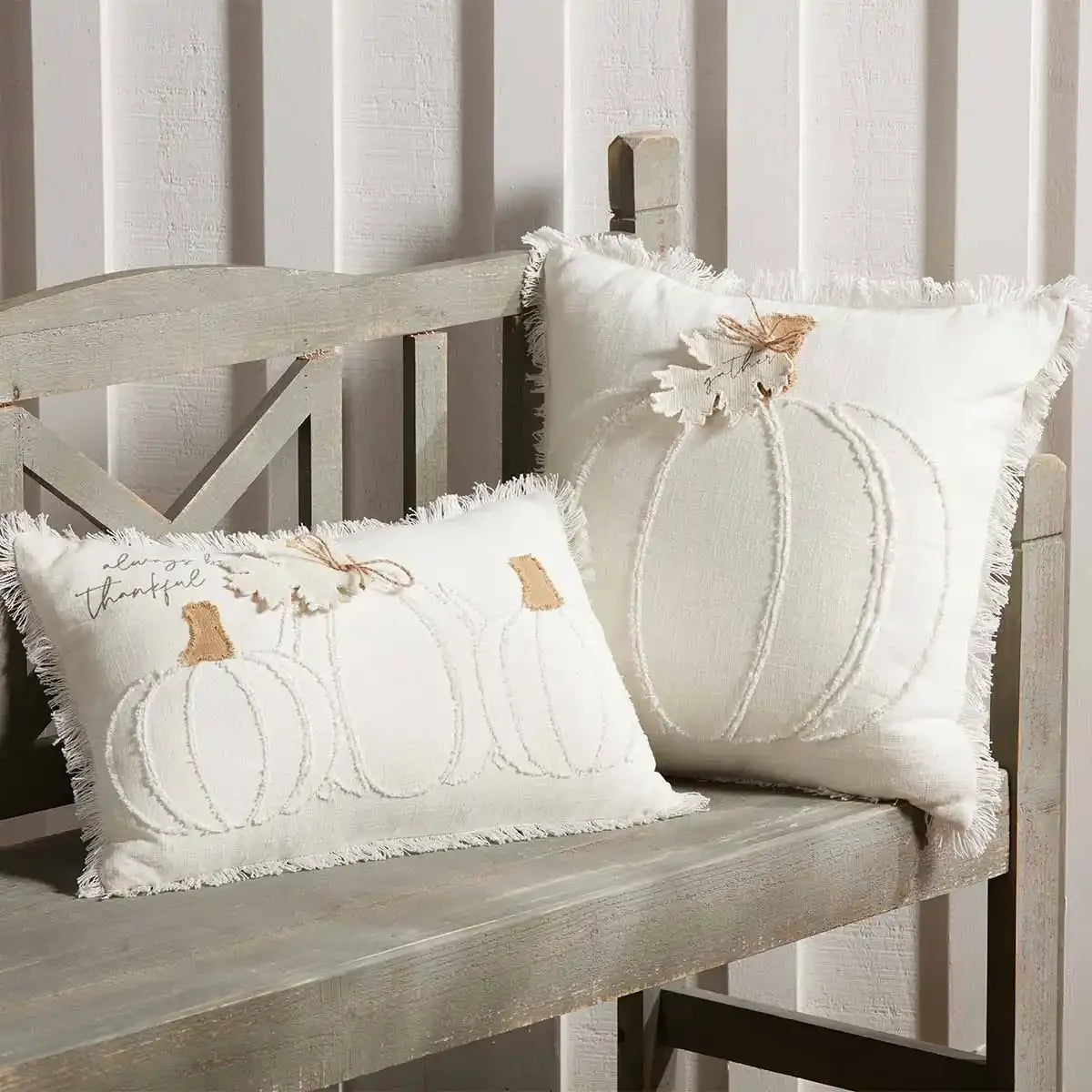 Two decorative white pillows with boho pumpkin designs on a rustic wooden bench