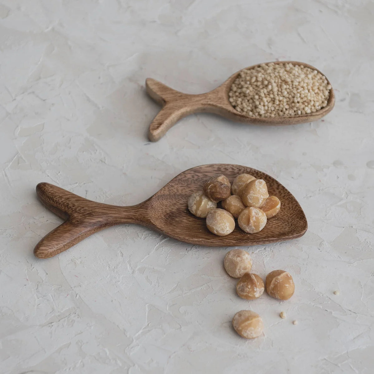 Two wooden spoons with nuts on an Acacia Wood Fish Shaped Dish, perfect for serving