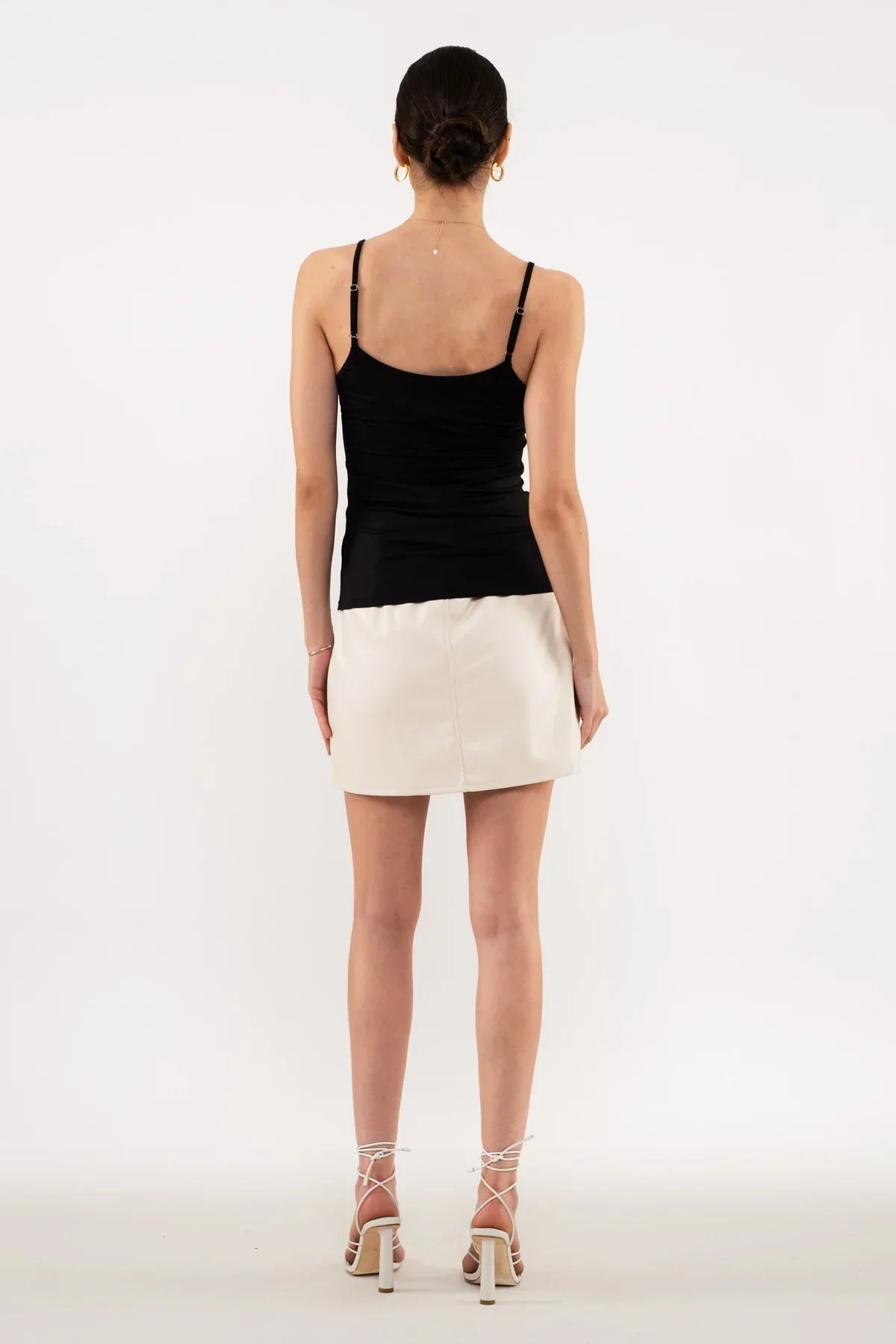 Back view of a model in a black spaghetti strap tank top and white mini skirt