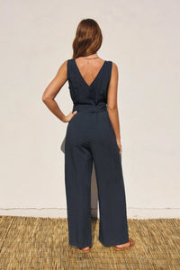 Back view of a woman in a navy BUTTON DOWN SASH BELT JUMPSUIT with v-neck button closures