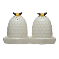 White ceramic beehive salt and pepper shakers with gold tops on a honeycomb plate