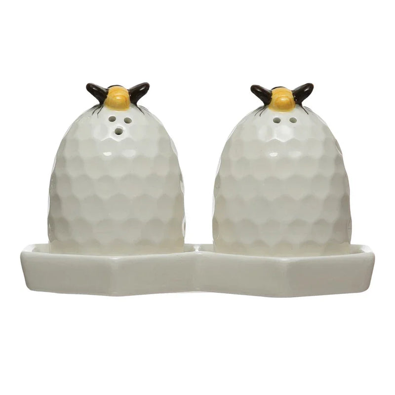 White ceramic beehive salt and pepper shakers with gold tops on a honeycomb plate