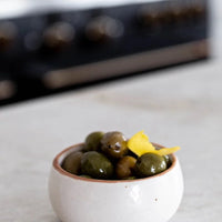 White speckled ceramic dip bowl with green olives and lemon zest