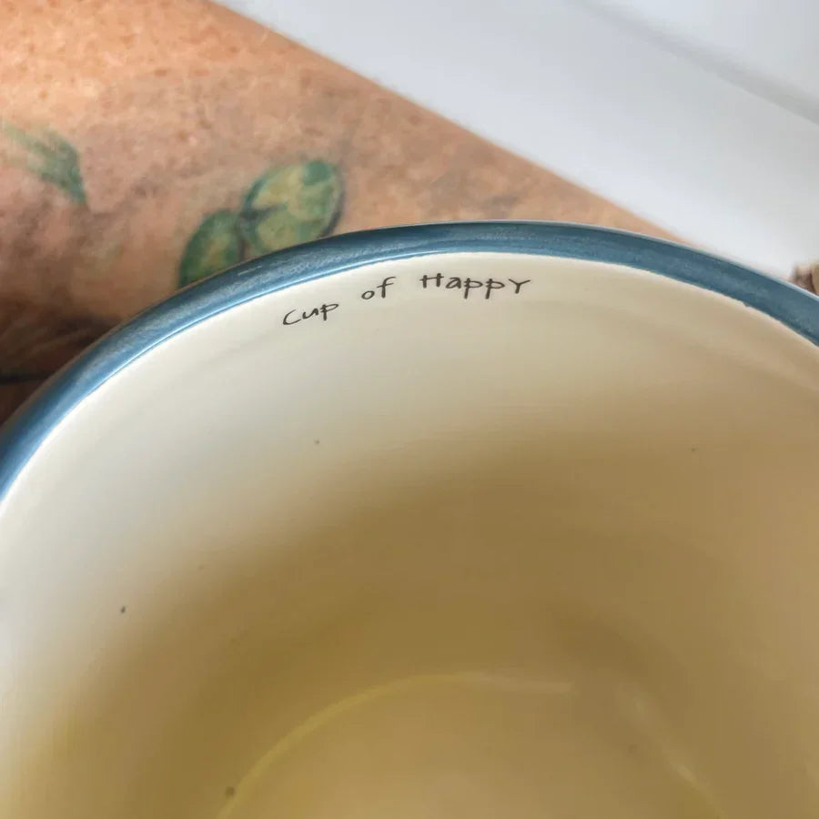 White ceramic mug with cup of happy, featuring hand sculpted narwhal folk art