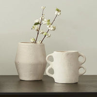 White ceramic vase with flowering branches and a boho double-handled cup beside it