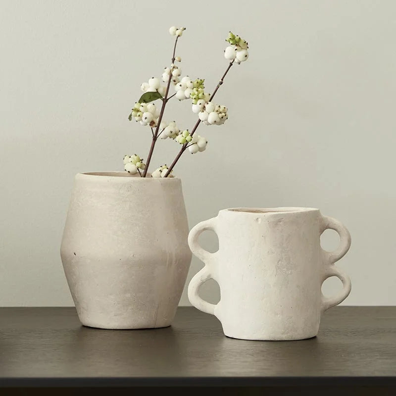 White ceramic vase with flowering branches and a boho double-handled cup beside it